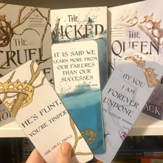 a person holding up four bookmarks in front of bookshelves