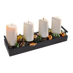 three white candles sitting on top of a tray filled with greenery and pine cones