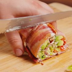 a person is holding a knife and cutting up a bacon wrapped sandwich with lettuce