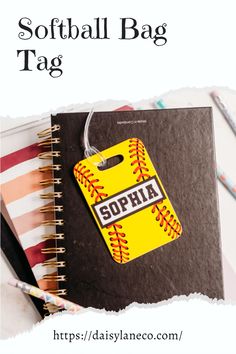 a softball bag tag on top of a notebook next to pencils and paper clips