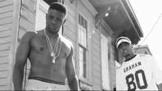 two black men standing next to each other in front of a house with one wearing a football jersey