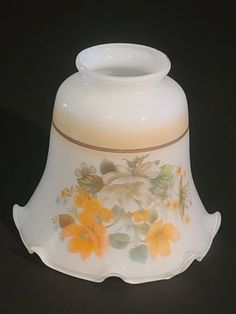 a white vase with yellow flowers painted on the side and brown trim around the bottom