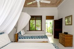 two beds in a bedroom with white sheets and blue bedding, along with a ceiling fan