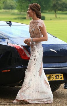 a woman in a long dress walking next to a car