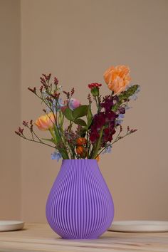 a purple vase filled with colorful flowers on top of a wooden table in front of a beige wall