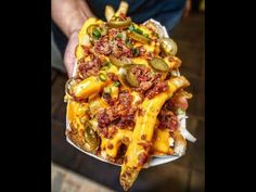 a person holding a plate full of cheesy pasta and pickles on it