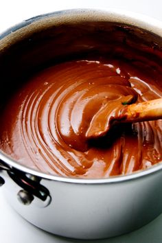 a pot filled with melted chocolate sitting on top of a table next to a wooden spoon