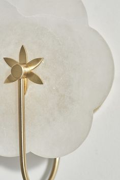 a white flower shaped light fixture with a gold metal hook on it's side