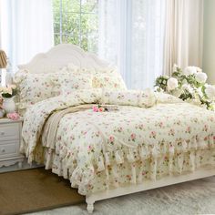 a white bed sitting next to a window with flowers on the covers and pillow cases