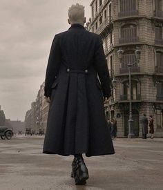 a man in a black coat is walking down the street with his back to the camera