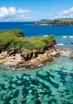 an aerial view of the ocean with rocks and green land in the foreground, surrounded by blue water