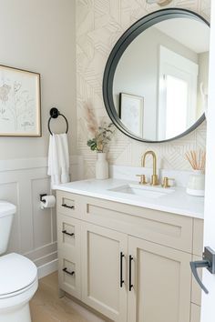 a bathroom with a toilet, sink and large round mirror above the vanity in it