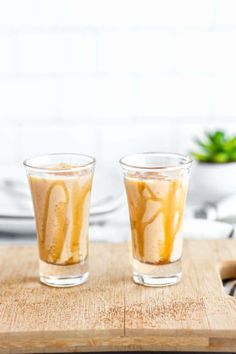 two glasses filled with liquid sitting on top of a wooden cutting board