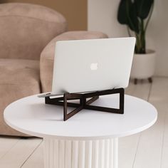 an apple laptop sitting on top of a white table next to a chair and potted plant