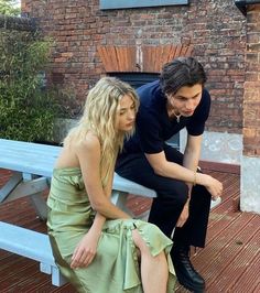 two people sitting on a bench in front of a brick building and one is looking down