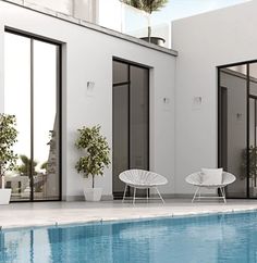 two white chairs sitting next to a swimming pool in front of a building with large windows