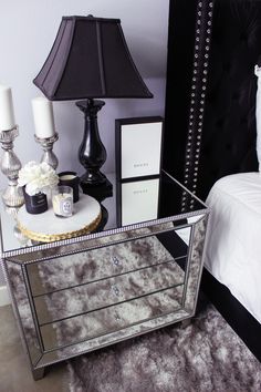 a mirrored table topped with a black lamp next to a white bed and two nightstands