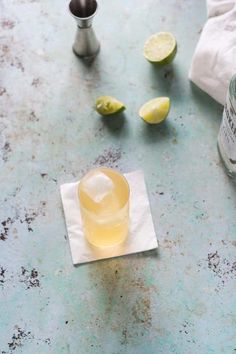 a glass filled with liquid sitting on top of a table next to some limes