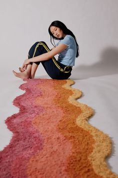 a woman is sitting on the floor with her legs crossed in front of an area rug