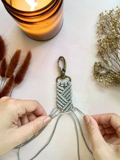 two hands holding a keychain made out of seed beads next to a candle