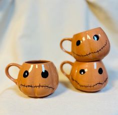 two coffee mugs with faces painted on them are sitting next to each other in front of a white sheet