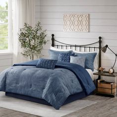 a bed with blue comforters and pillows in a room next to a plant on a table