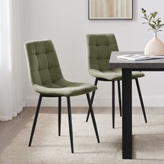 two green chairs sitting at a table in front of a vase with flowers on it