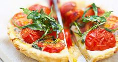 two small pizzas with tomatoes and basil on them are cut in half to eat