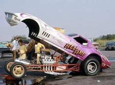 an old drag car is parked in a parking lot with people looking at the cars