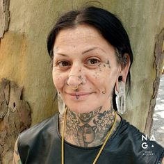 a woman with tattoos and piercings standing next to a tree