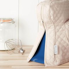 a white backpack sitting on top of a wooden floor next to a glass jar filled with milk