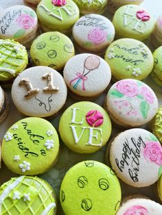 many decorated cookies with writing on them are displayed in a plate, one is green and the other is pink