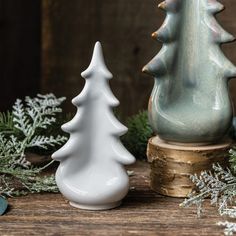 two ceramic christmas trees sitting next to each other on top of a wooden table with greenery