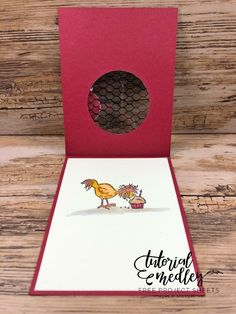 an open card with a rooster and bird on the front, inside it is a red envelope