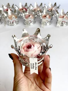 a hand holding a small silver crown with pink flowers on it and price tag in front of them