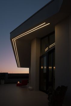 a building that has lights on the side of it at night, and there is a red chair outside