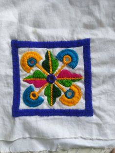 an embroidered square on a white cloth with blue border and multicolored flowers in the center