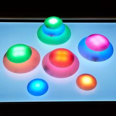 four different colored balls sitting on top of a white surface with black light in the background