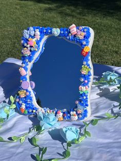 a blue mirror sitting on top of a table covered in flowers and leaves next to a green grass field