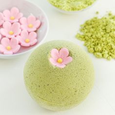 there is a green bath bomb with pink flowers on it next to other small bowls