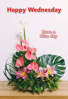 a vase filled with pink flowers on top of a wooden table next to green leaves