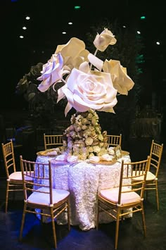 an arrangement of flowers on a table with chairs around it at a wedding reception in the dark