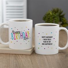 two coffee mugs sitting on top of a wooden table with the words happy birthday written on them