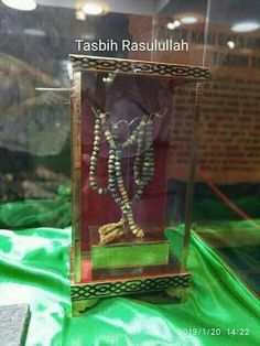 a glass case with beads in it sitting on a green cloth covered table next to a brick wall