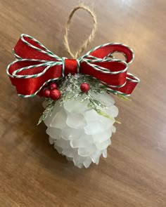 a christmas ornament hanging on a wooden table with red ribbon and holly berries