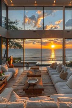 a living room filled with lots of white furniture and windows overlooking the ocean at sunset