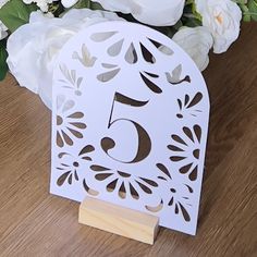 there is a white paper cutout with the number five on it and flowers in the background