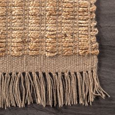 an area rug with fringes on top of wooden flooring and dark wood background