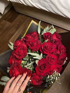 a bouquet of red roses sitting on top of a table next to a person's hand