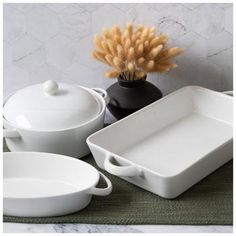 white dishes are sitting on a green tablecloth with wheat stalks in the vase behind them